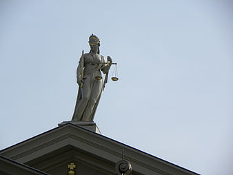 Lady Justice Statue on Courthouse Roof Against Blue Sky
