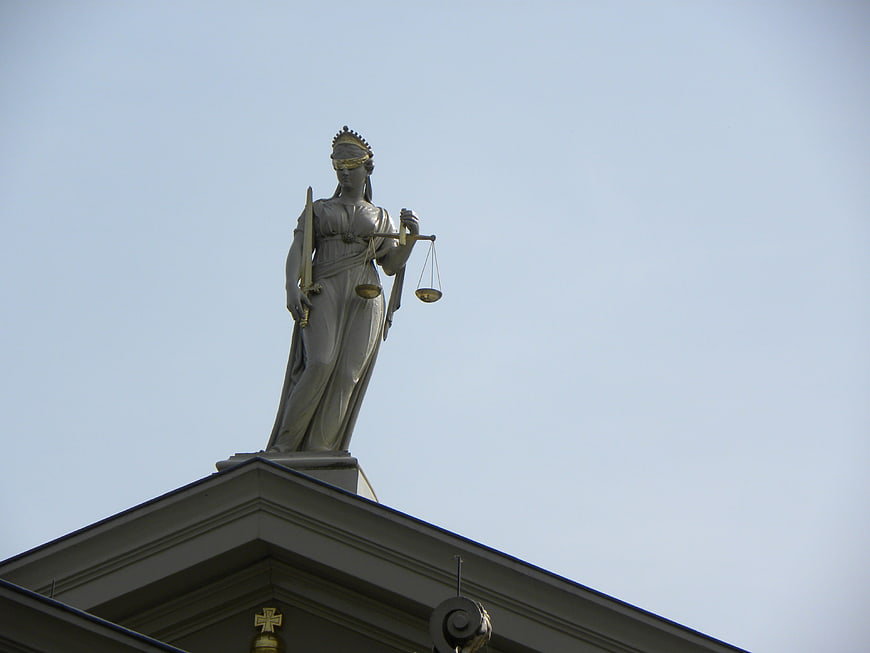 Lady Justice Statue on Courthouse Roof Against Blue Sky