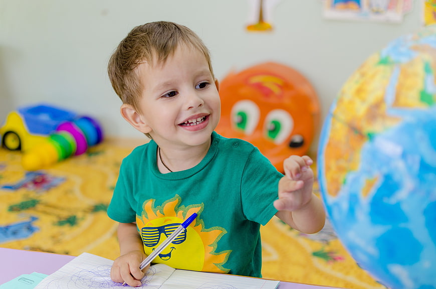 Happy toddler boy drawing with pen at table with globe
