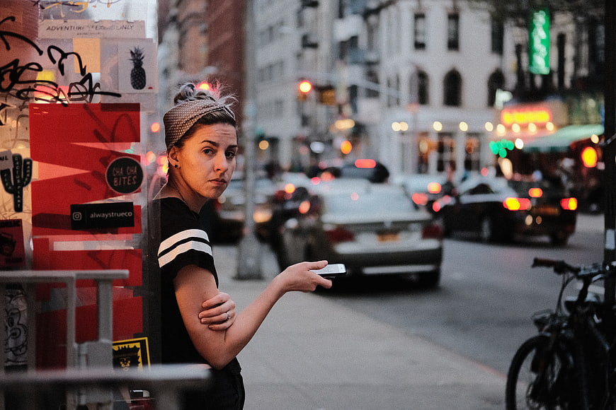 Woman waiting on busy city street holding smartphone