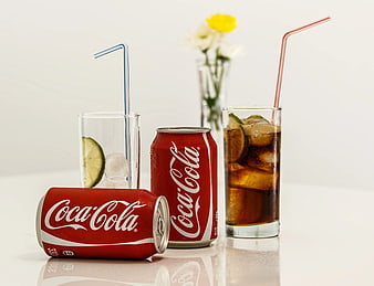 Coca-Cola cans and glasses with ice and lime on white background