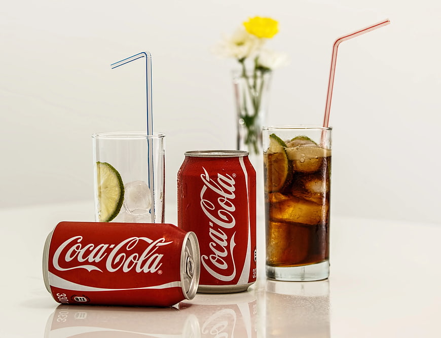 Coca-Cola cans and glasses with ice and lime on white background