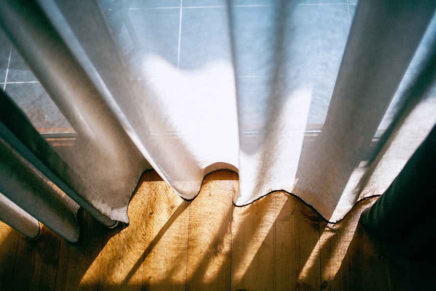 Sunlight streaming through sheer curtains onto wooden floor