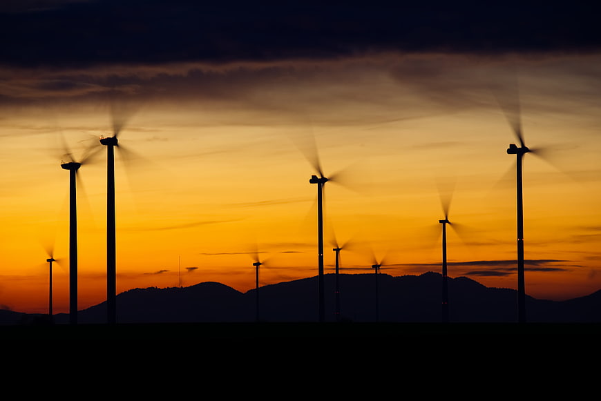 Silhouetted Wind Turbines Against Vibrant Orange Sunset Sky