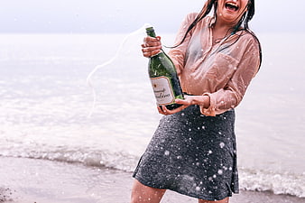 Woman celebrating on beach popping champagne bottle