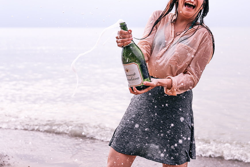 Woman celebrating on beach popping champagne bottle