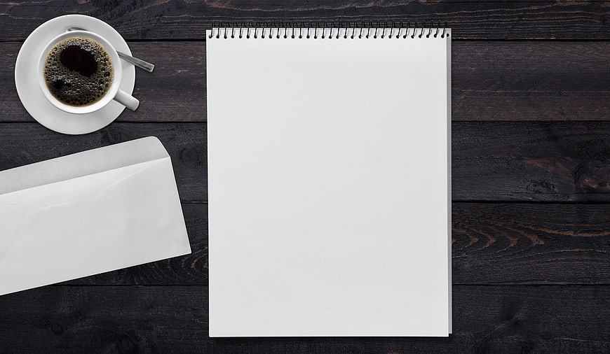 Flat lay of blank notepad, coffee cup, and envelope on dark wood