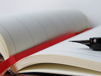 Close-up of fountain pen on open notebook with red ribbon