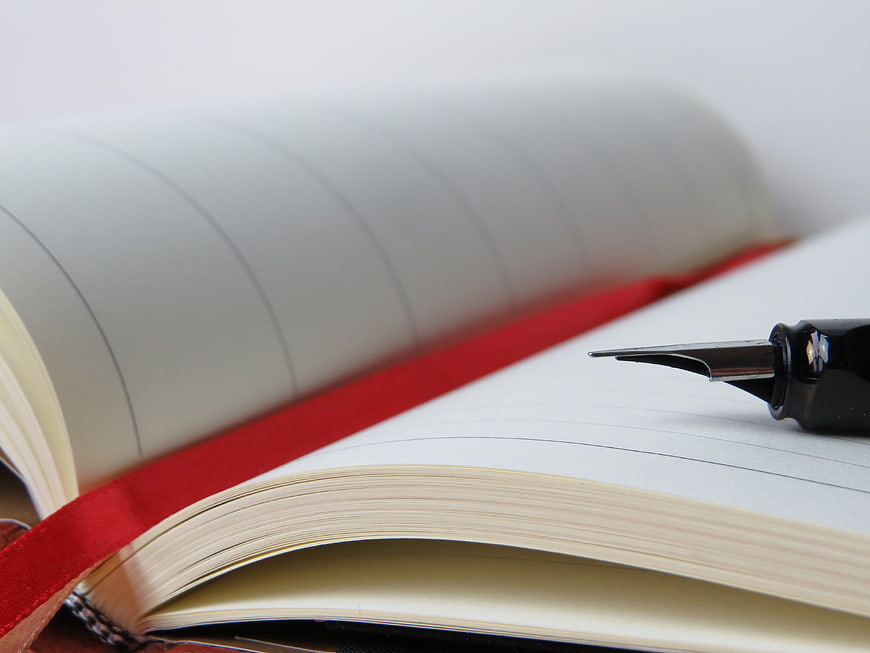 Close-up of fountain pen on open notebook with red ribbon