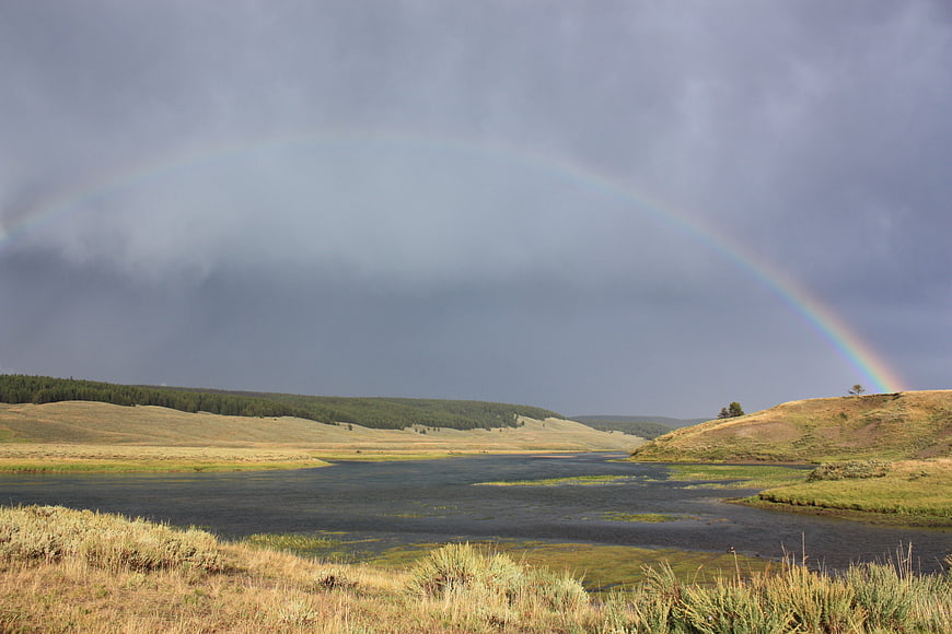 Vibrant Rainbow Arching Over Serene River and Rolling Hills