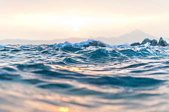 Close-up of ocean waves at sunset with blurred mountains