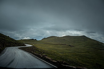 Winding wet road through green hills under stormy sky