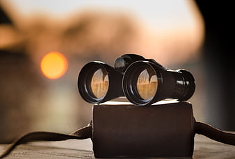Black binoculars on leather case with sunset bokeh background