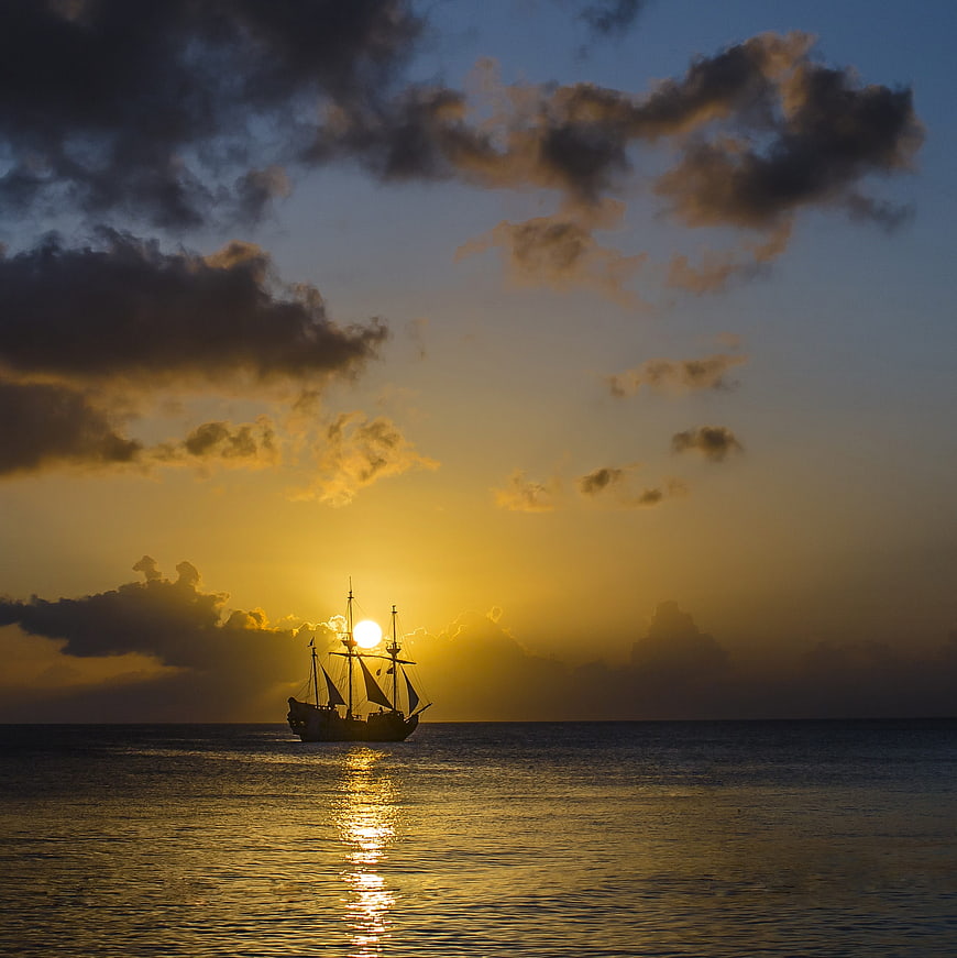 Silhouette of sailing ship on ocean at golden sunset