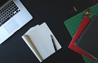 Flat lay workspace with laptop, notebook, and books on black desk