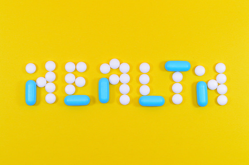 Health word spelled with white and blue pills on yellow background