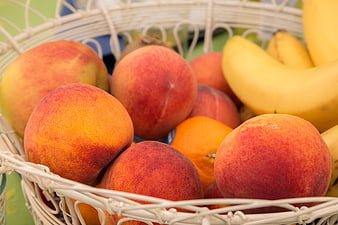 Ripe peaches and bananas in a white woven fruit basket
