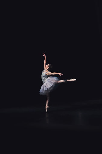 Ballerina performing arabesque on dark stage