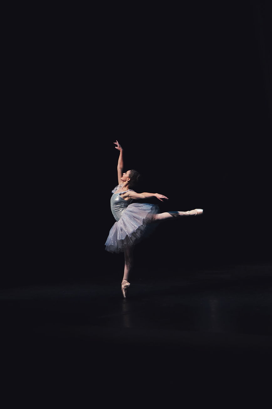 Ballerina performing arabesque on dark stage