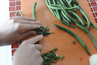 Hands chopping fresh green beans on orange cutting board