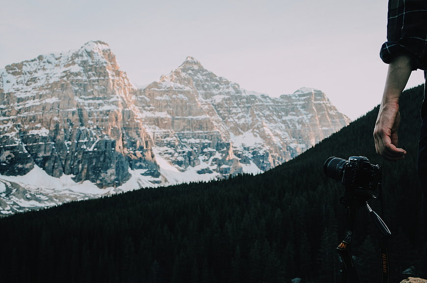 Photographer with Camera on Tripod Facing Snowy Mountain Peaks