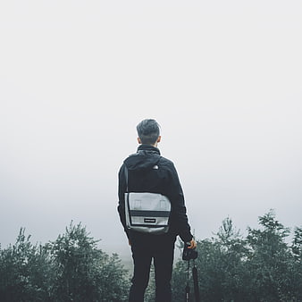 Man with Backpack and Camera Standing on Misty Mountain Peak