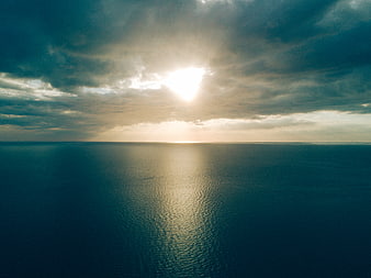 Sunlight breaking through clouds over calm ocean horizon