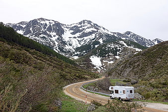 White Motorhome Parked On Winding Mountain Road With Snowy Peaks