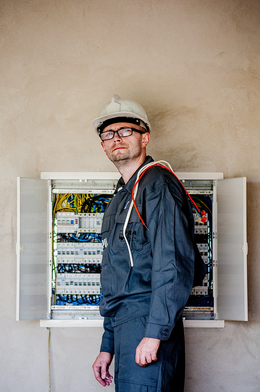 Electrician in Hard Hat Standing by Open Electrical Panel