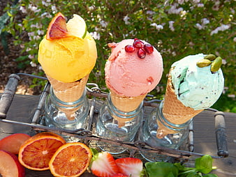 Three colorful fruit sorbets in cones with fresh garnishes