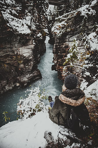 Woman sitting on snowy cliff overlooking icy canyon river