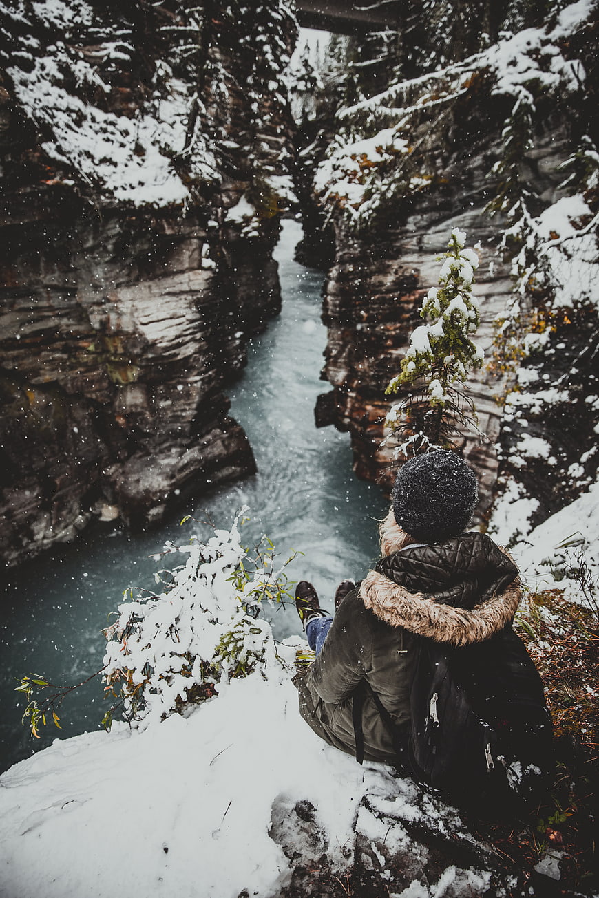 Woman sitting on snowy cliff overlooking icy canyon river