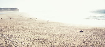 Wide sandy beach with people walking and relaxing near ocean waves