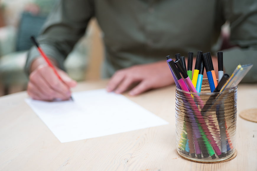 Person writing with colorful markers on wooden table