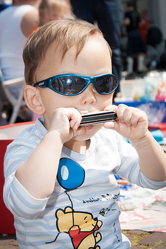 Toddler boy wearing sunglasses playing harmonica outdoors