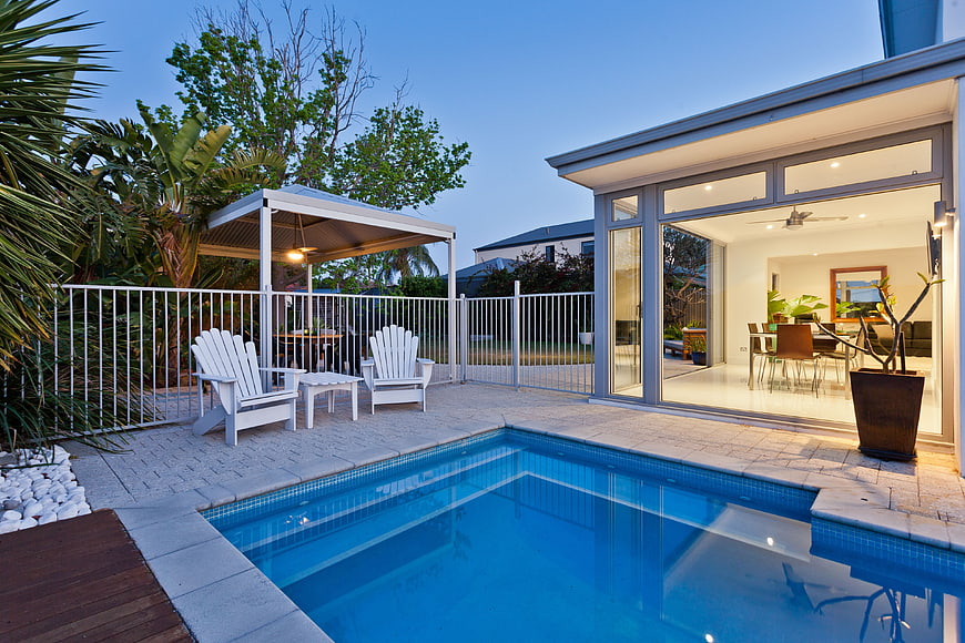 Modern Backyard Patio With Swimming Pool And Open Glass Doors At Dusk