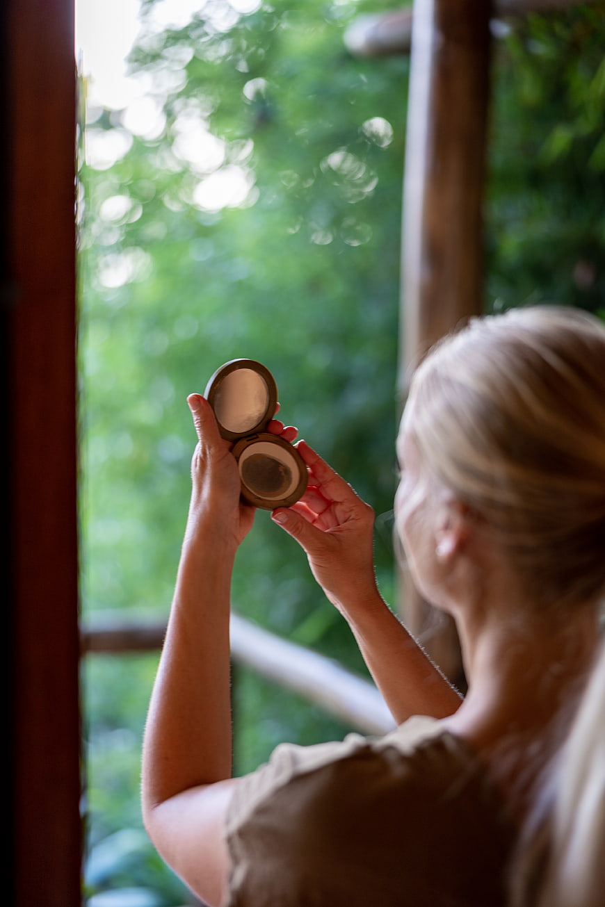 Woman applying makeup with compact mirror near window