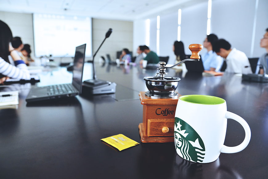 Coffee Mug and Grinder on Conference Table with Blurred Meeting Background