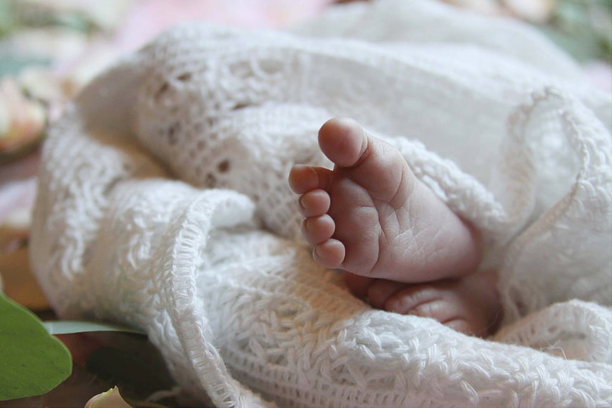 Close-up of newborn baby feet wrapped in white knit blanket