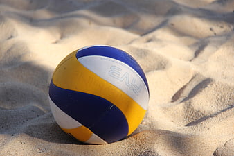 Blue and yellow volleyball resting on sandy beach