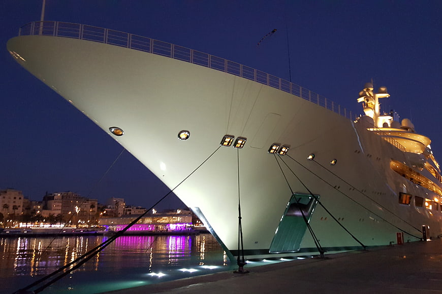 Massive white superyacht docked at night with city lights