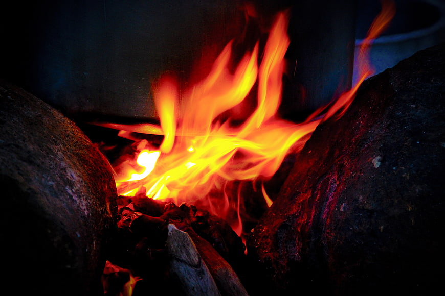 Close-up of bright orange flames burning between dark rocks