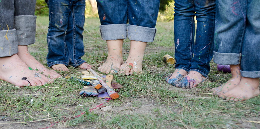 Bare feet with paint splatters on grass with brushes