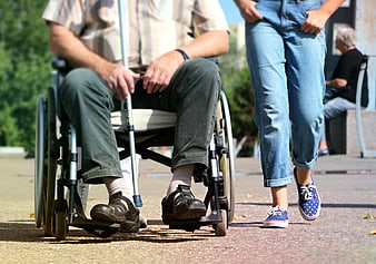 Senior man in wheelchair walking with young woman outdoors