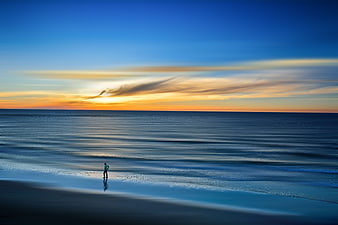 Solitary figure walking on a calm beach at sunset with long exposure water