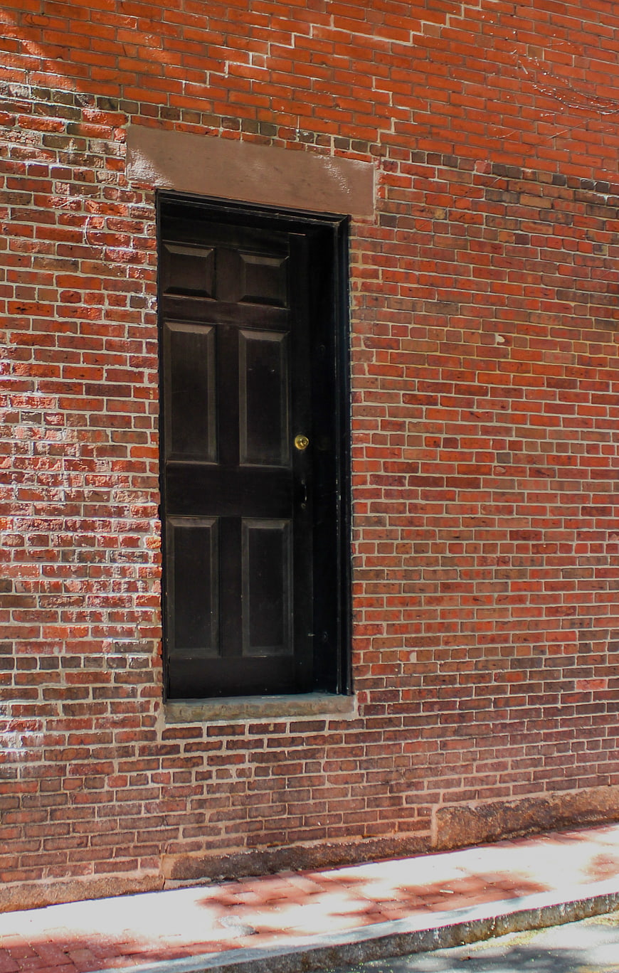 Black door on red brick wall with sidewalk