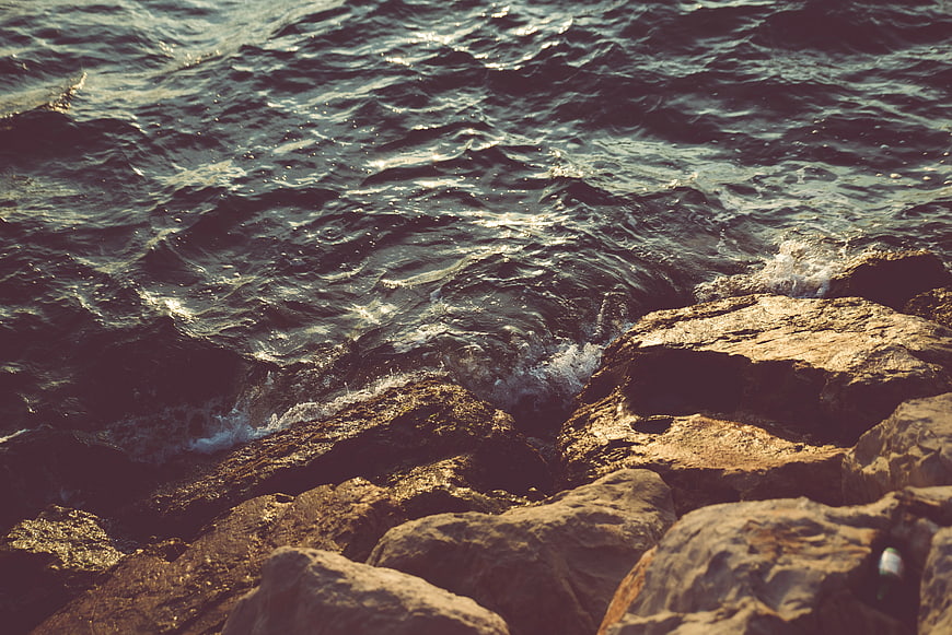 Dark ocean waves crashing on sunlit rocky coast