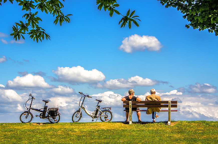 Senior couple sitting on a bench with bicycles on a grassy hill