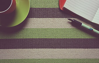 Flat lay of coffee cup, notebook, and pen on striped placemat
