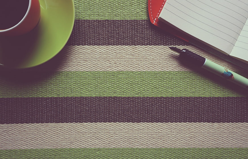 Flat lay of coffee cup, notebook, and pen on striped placemat